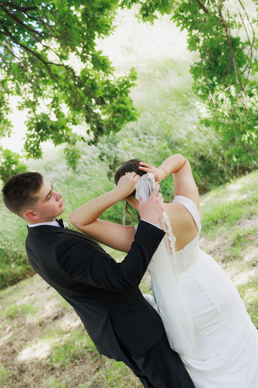 Groom helping his bride with her veil under a tree